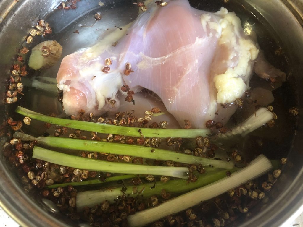 poach chicken thighs in water with ginger and scallion in a pot