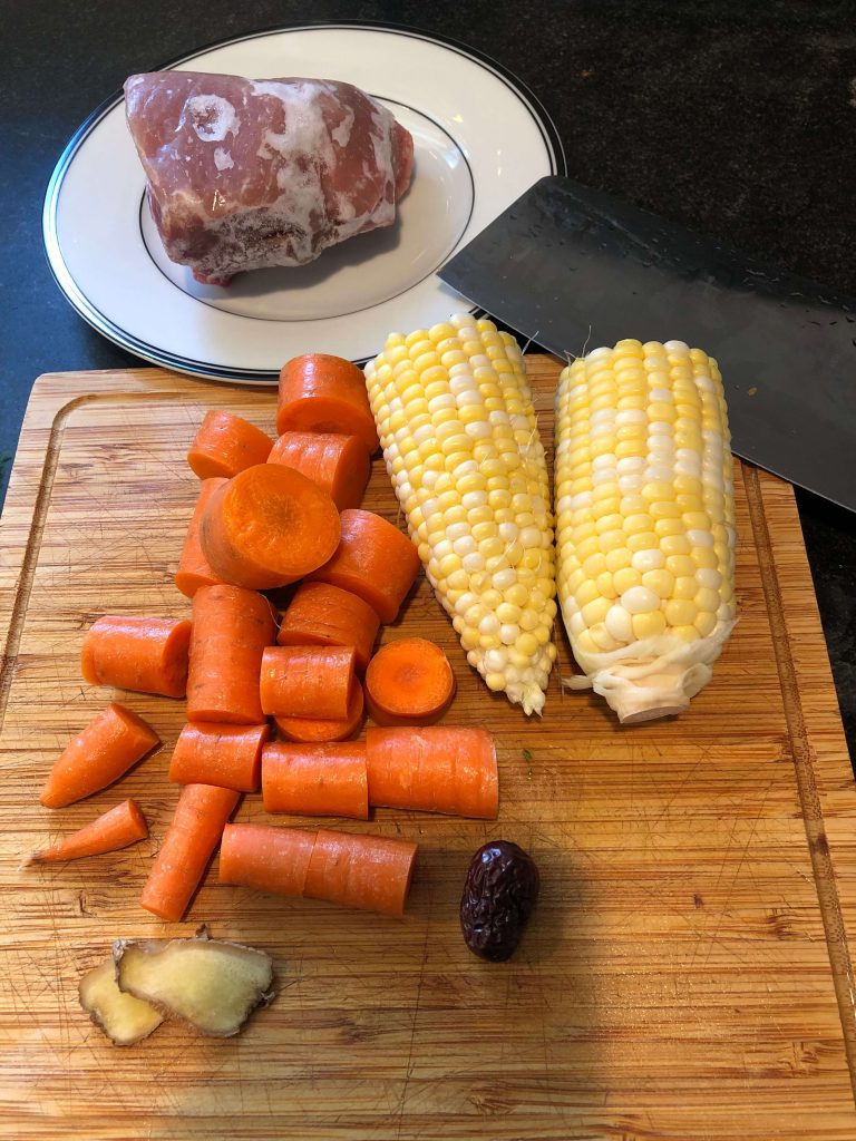Cut corn, carrots and ginger, date on a cutting board. Pork on a plate.